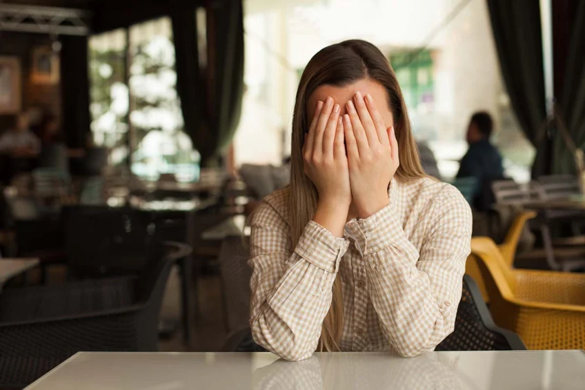 woman with hands over face at table dealing with types of addiction