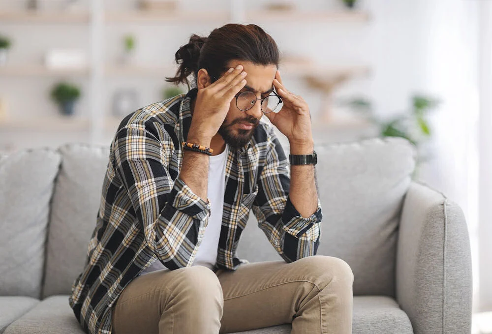 man holding head upset on couch