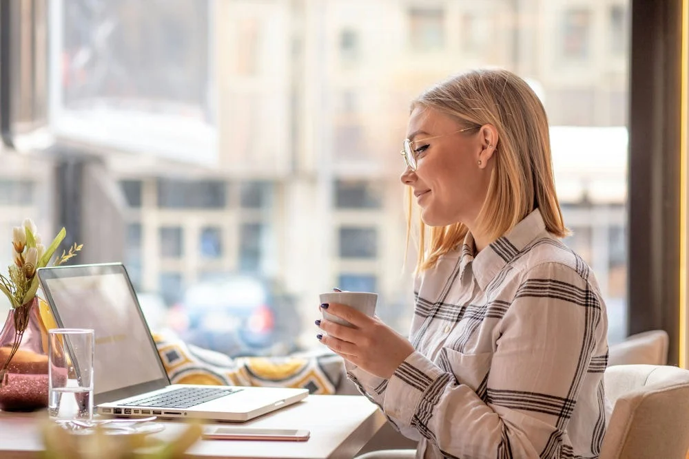 a woman smiling with a cup of coffee on laptop