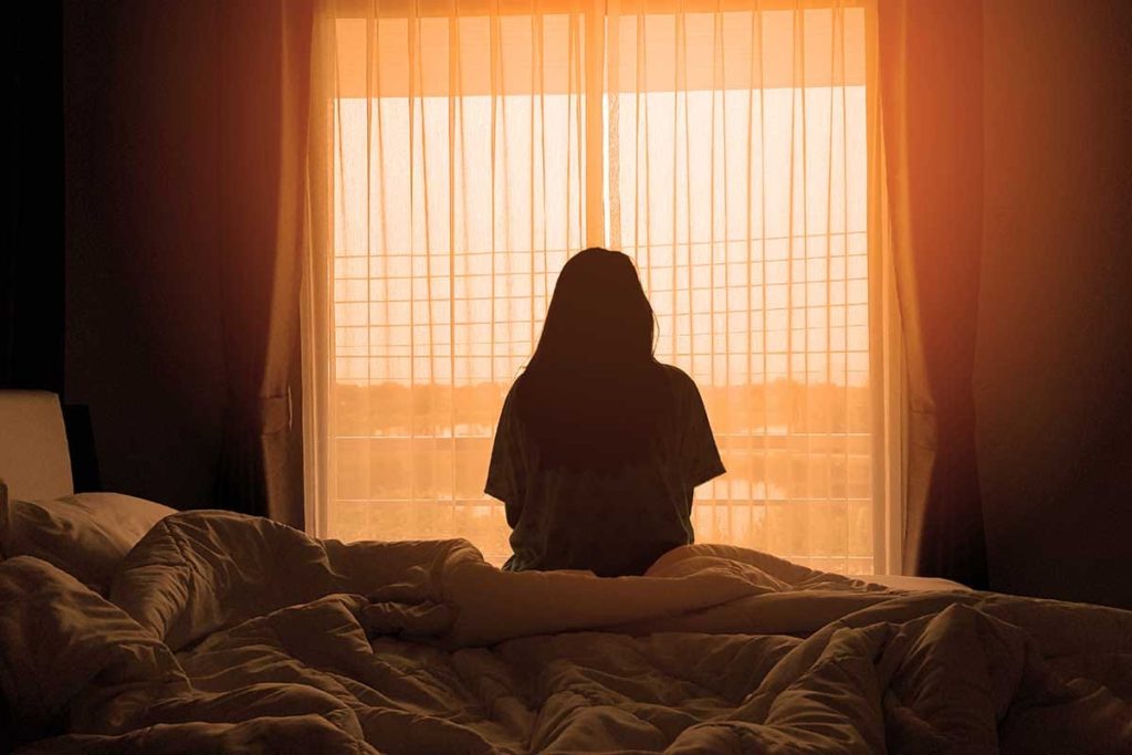 woman sitting on bed wondering how long heroin withdrawal lasts