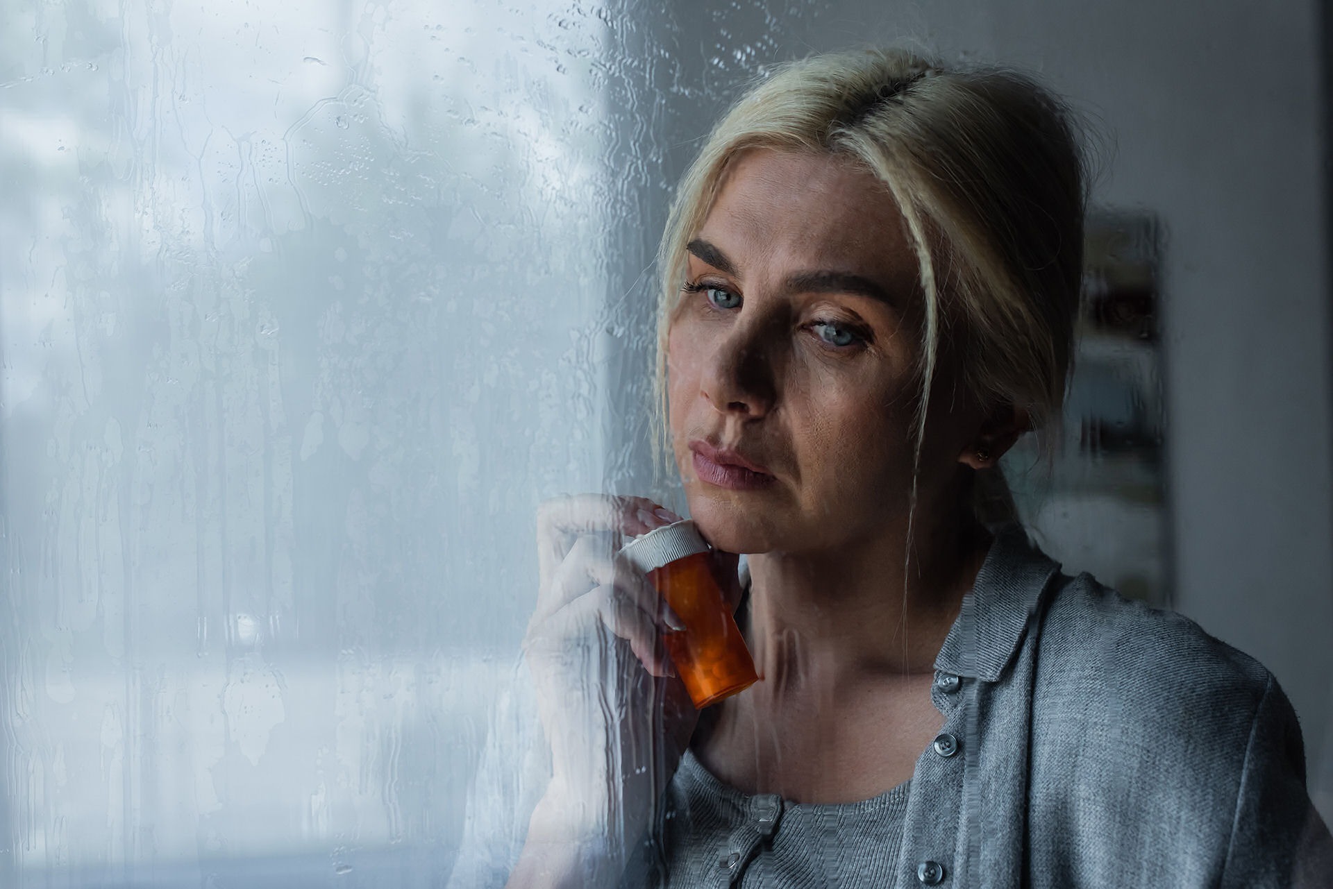 a woman leaning on window sill with a pill bottle