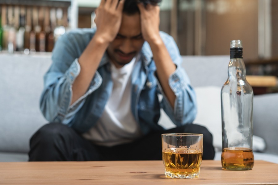 a man stressed out in front of a glass of whiskey